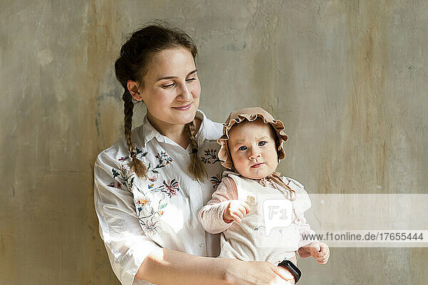 Smiling mother with cute daughter standing in front of wall