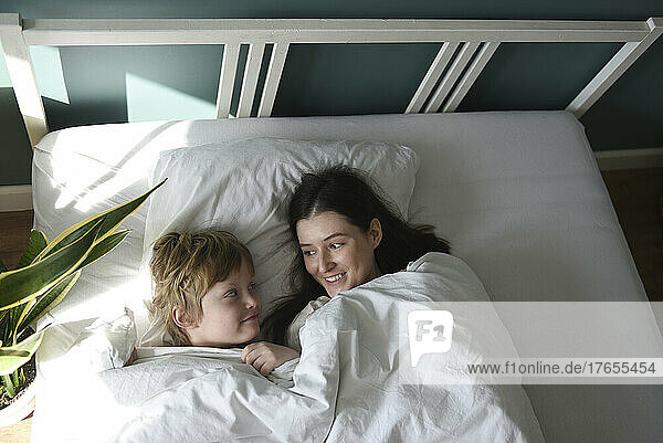 Mother and son with blanket lying in bed at home