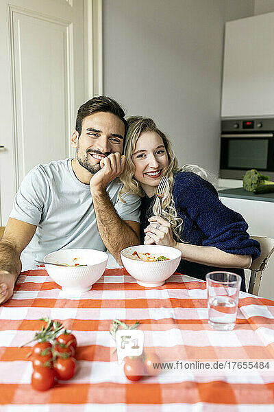 Man with hand on chin sitting with girlfriend on dining table at home
