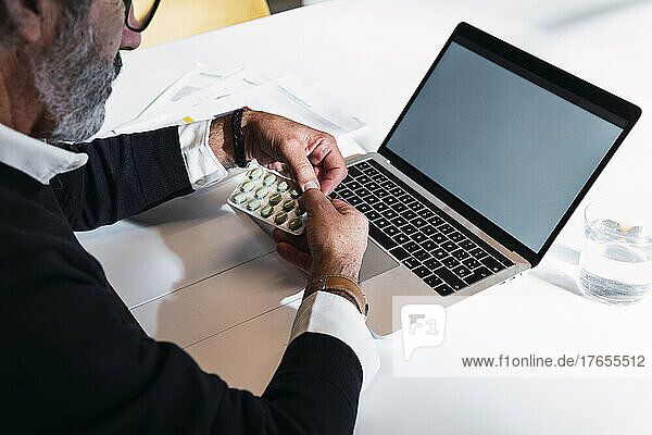 Freelancer removing pills sitting with laptop at table