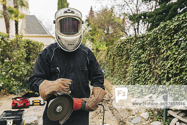 Man wearing welding helmet standing with grinder at construction site