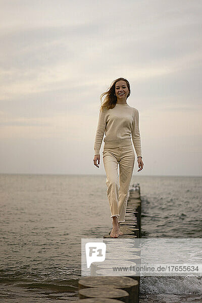Lächelnde Frau  die auf einem Holzpfosten am Strand läuft