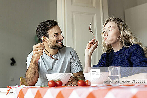 Mann schaut Freundin beim Essen zu  die zu Hause am Esstisch sitzt