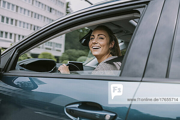 Happy young woman looking through car window at road