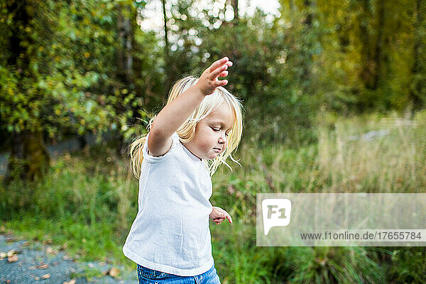 Young blonde girl using arms to balance  playing outdoors.