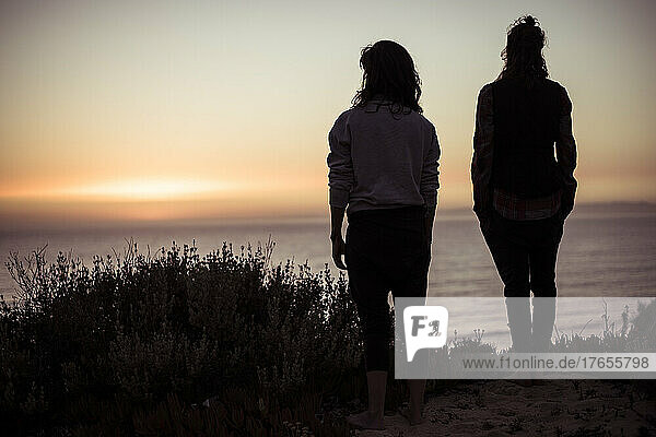 Silhouette of two women on ocean cliff watching sunset in Portugal