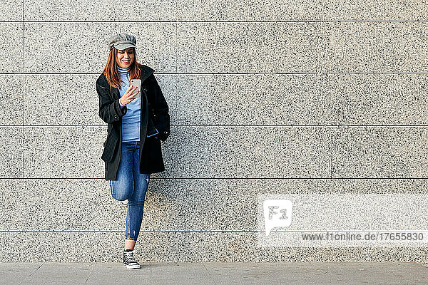 Woman with phone and casual clothes leaning against a wall. Copy space