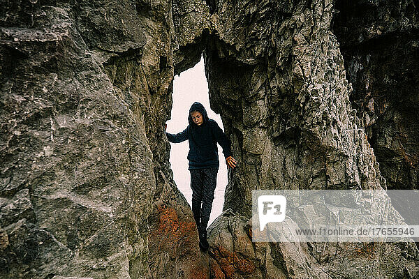 Hooded Teen Crawls Through Rock Crevice on Northwest Coast