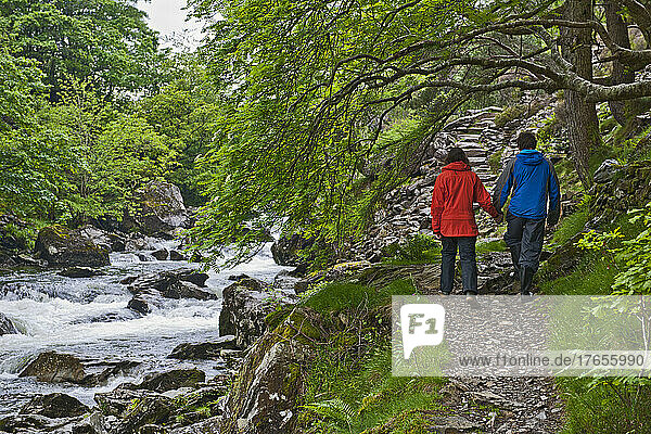 Couple walking hand in hand along a stream at Snowdonia National Park