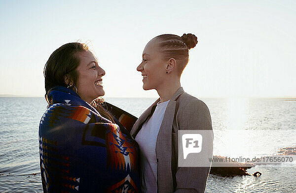 lesbian couple laughing together at the beach at sunset