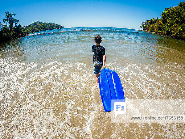 Boy walking into ocean with boogie board on vacation in Costa Rica.
