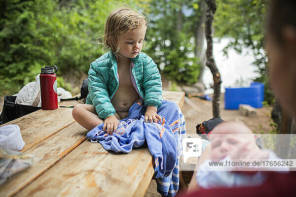A young child sits on picnic table ta campsite with baby