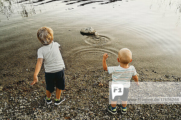 Back view of kids throwing pebbles in water in summer