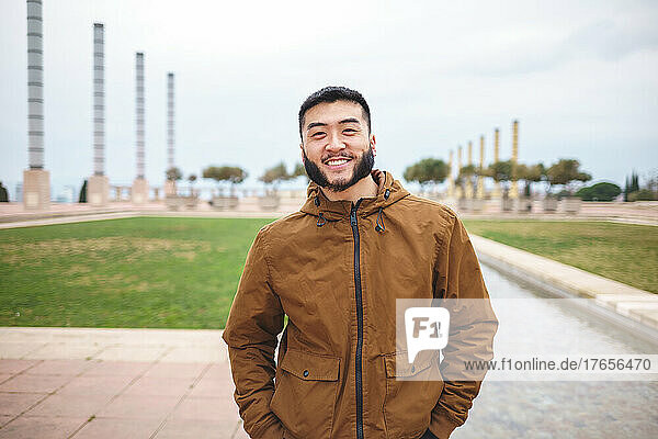 Smiling Asian man standing in park on cloudy day