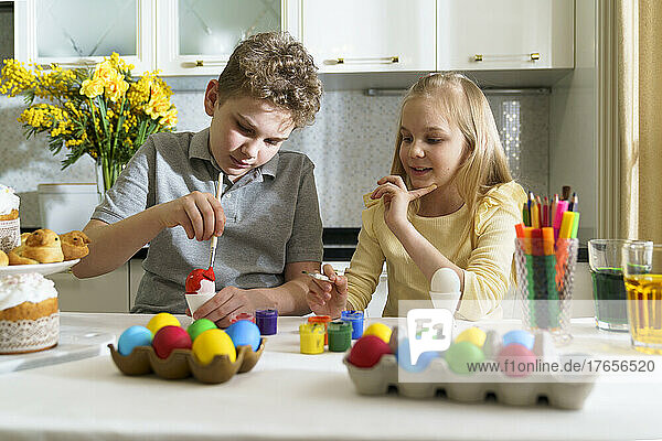 Cute brother and sister paints Easter eggs.