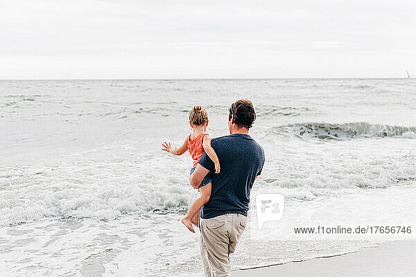 Father holds young daughter while watching the ocean waves