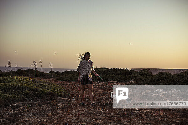 person walks two chihuahuas at sunset along ocean cliffs in Portugal