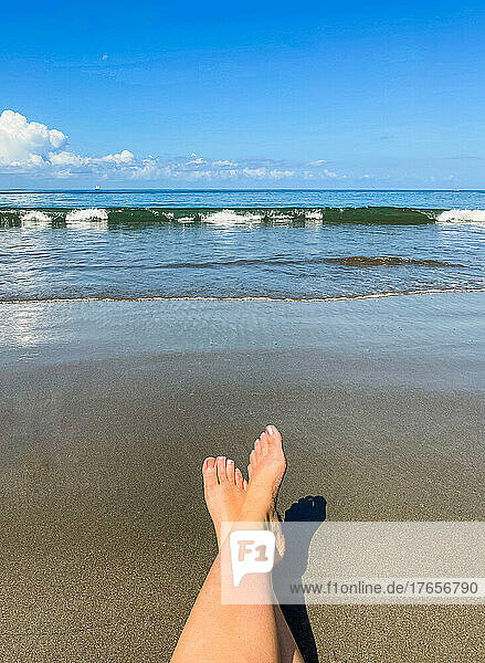 Woman's outstretched feet relaxing on the beach against the ocean.
