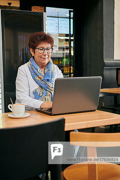 Mature woman working remotely with her laptop in a coffee shop