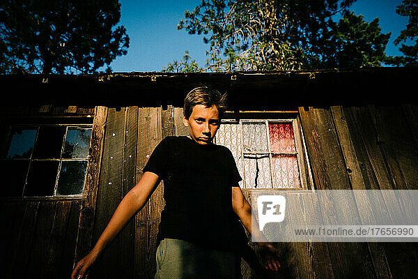 Teen Boy Stares Intensely into Camera at Golden Hour Next to Old Shed