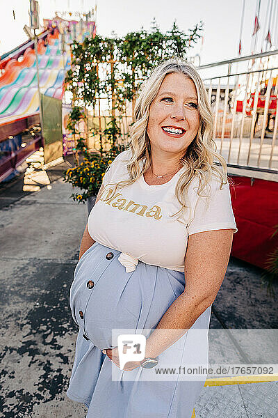 Pregnant Caucasian mother smiles in front of carnival rides