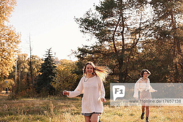 Two happy teenage girls smiling while running in forest in autumn