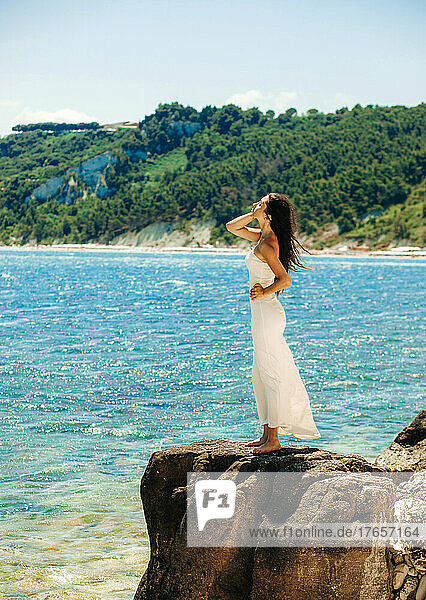 Gorgeous woman in a white dress stands on a stone against the ba