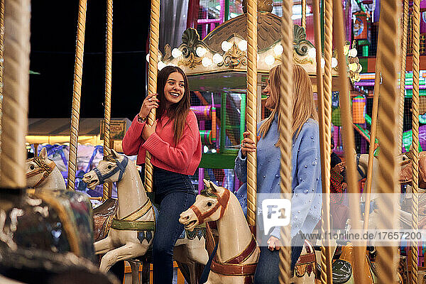 Two smiling young women ride on a carousel