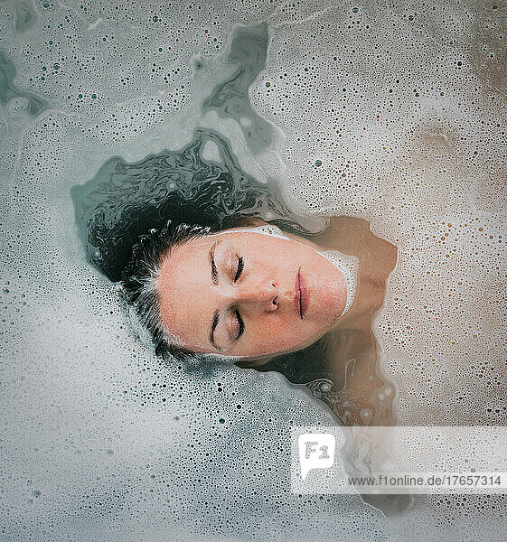 Overhead of woman relaxing in a bubble bath with eyes closed.