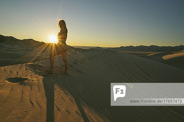 Naked female posing on the sand dunes with sunburst