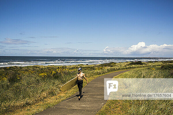 A man carrying a surfboard walks down a path toward the beach