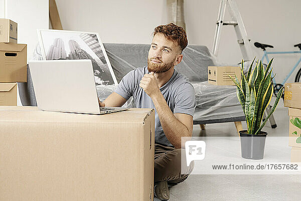 A young man sitting on the floor of his new home using his laptop.