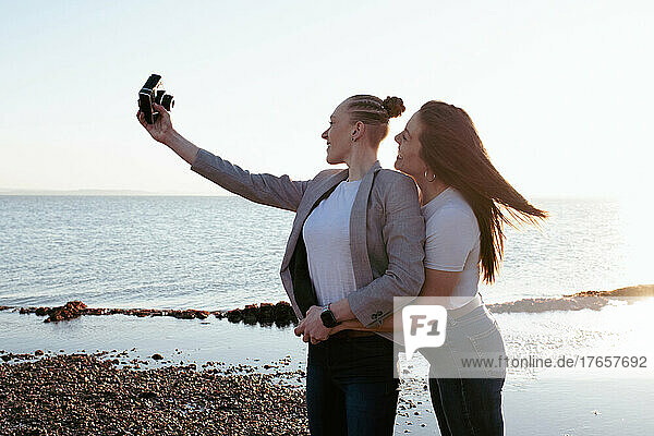 lesbian couple taking selfies at the beach at sunset