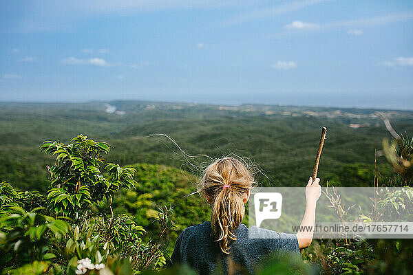 Blond girl overlooks green hills she hikes with blue sky