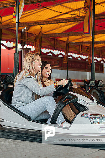 Two young women drive a bumper car while they are smiling