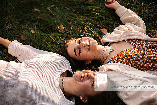 Two happy young women smiling while lying on grass