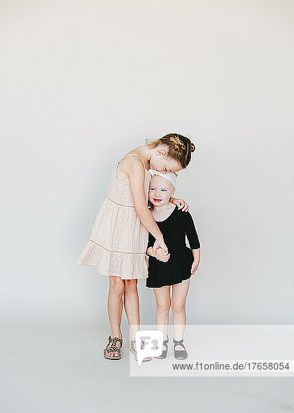 older sister kissing her younger sister in front of a white wall