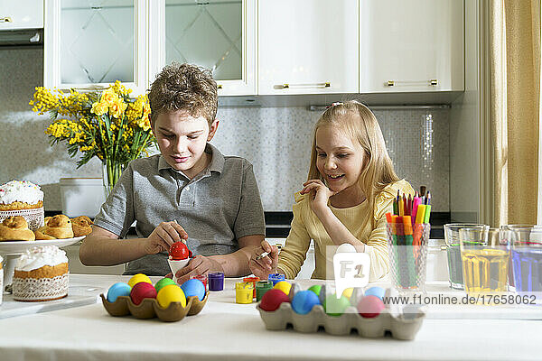 Laughing brother and sister paints Easter eggs.