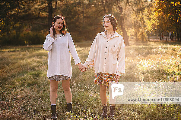 Two young women holding hands while standing in park during autumn