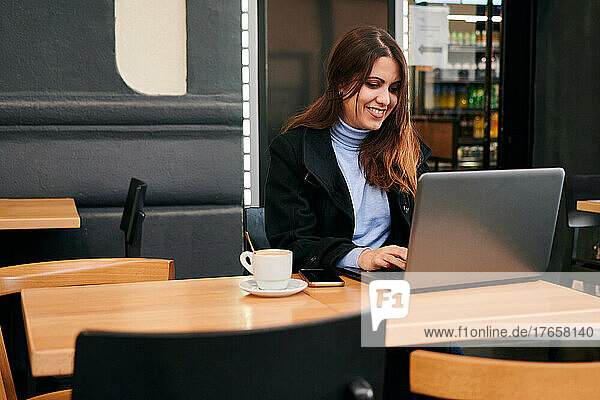 Woman working remotely with her laptop in a coffee shop