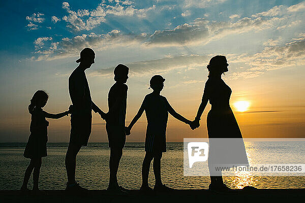 Mother and four children silhouetted against an ocean sunset