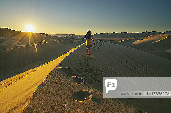 Naked female walking on a sand dune