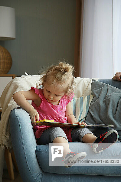 Little girl sits in a chair and looks at a book