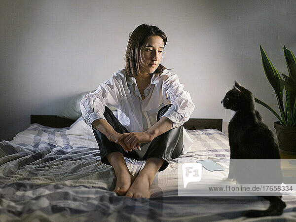 Woman sitting on the bed in the evening with a cat
