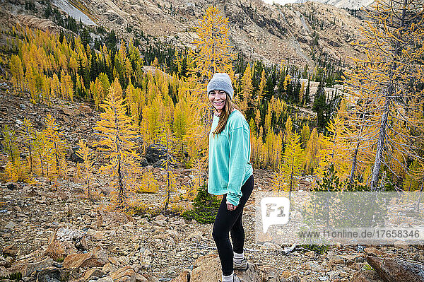Happy female hiker posing in a forest of golden larches in the fall