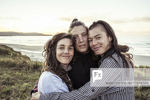 Three close strong female friends hug by the ocean