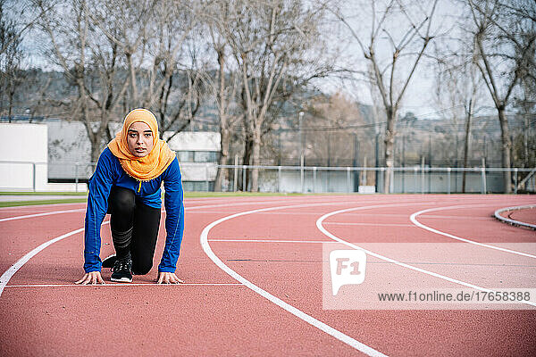 Serious ethnic woman in ready position on running track