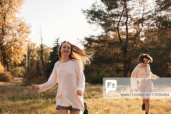 Two happy young women smiling while running in forest in autumn