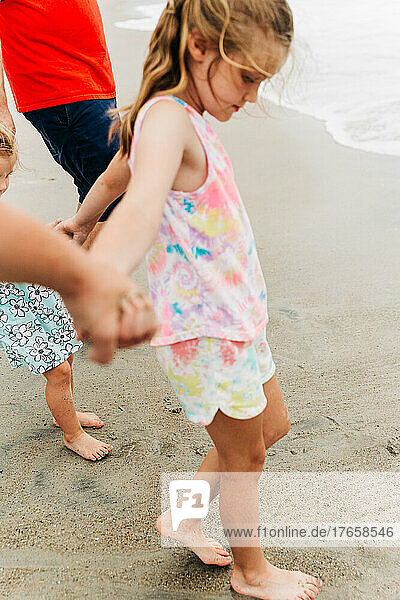 Young girl holding hands with her family while on the beach