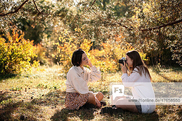 Young woman photographing girlfriend in park during autumn